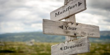 manifest your dreams text quote on wooden signpost outdoors in n